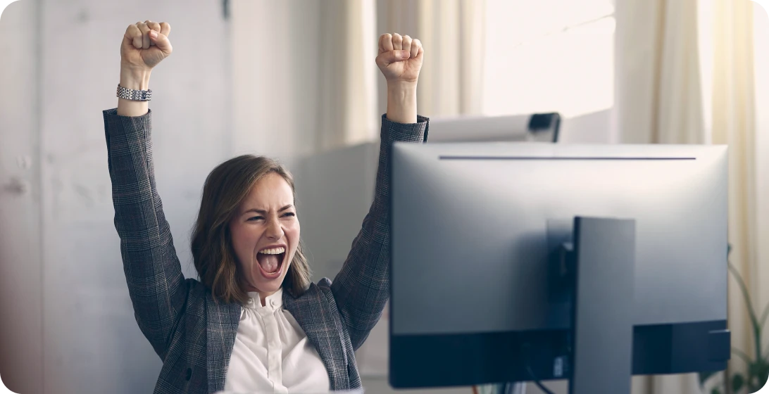 Frau freut sich im Büro vor ihrem Computer
